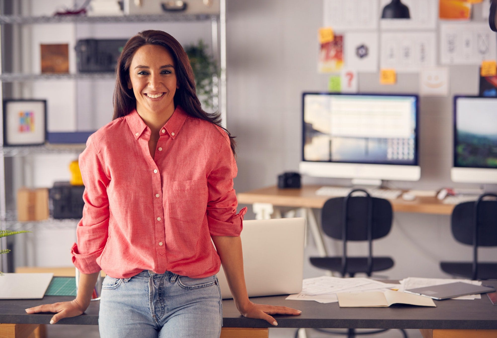 Portrait Of Female Advertising Marketing Or Design Creative In Studio Sitting On Desk